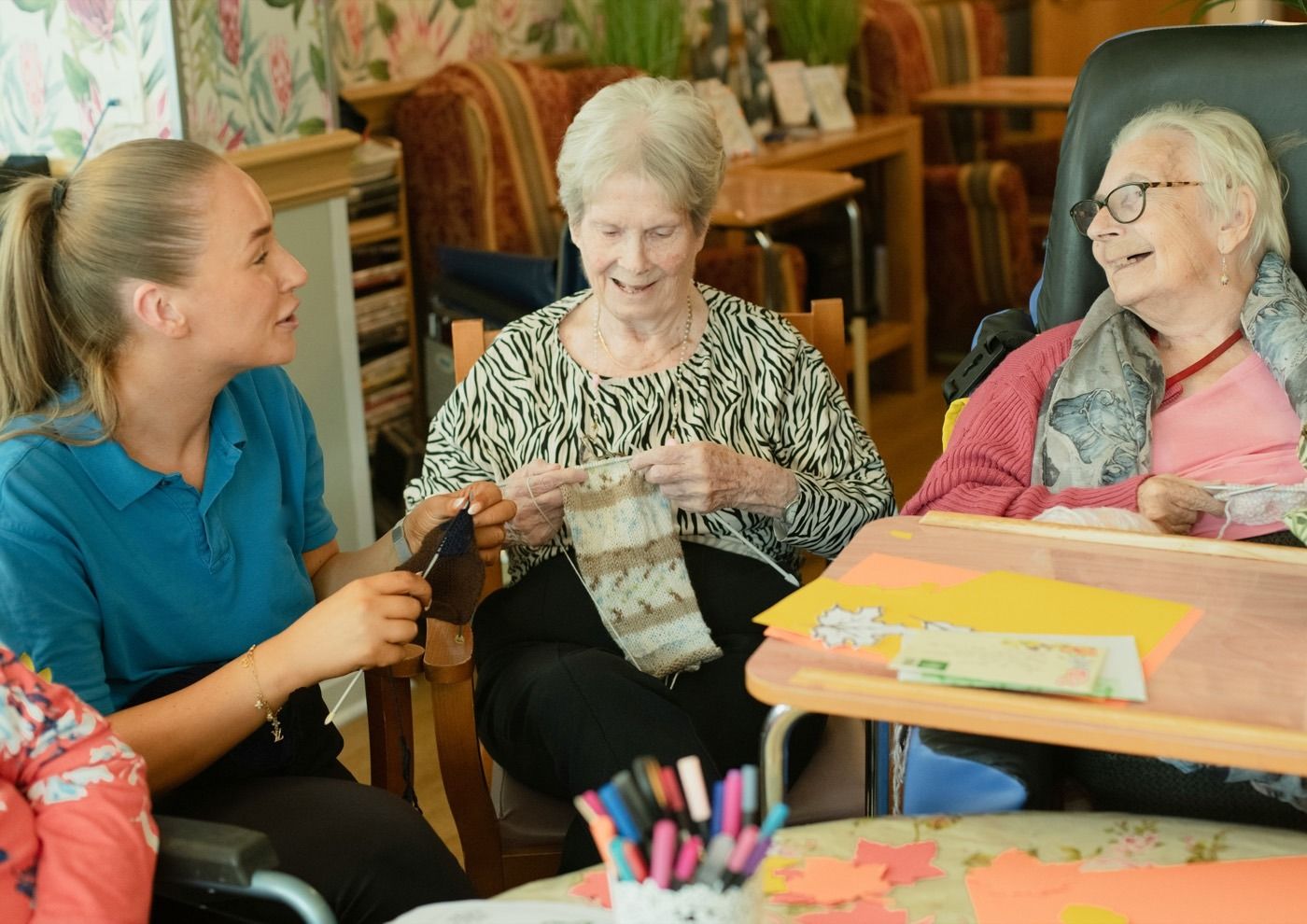 A caregiver knitting and laughing with two residents