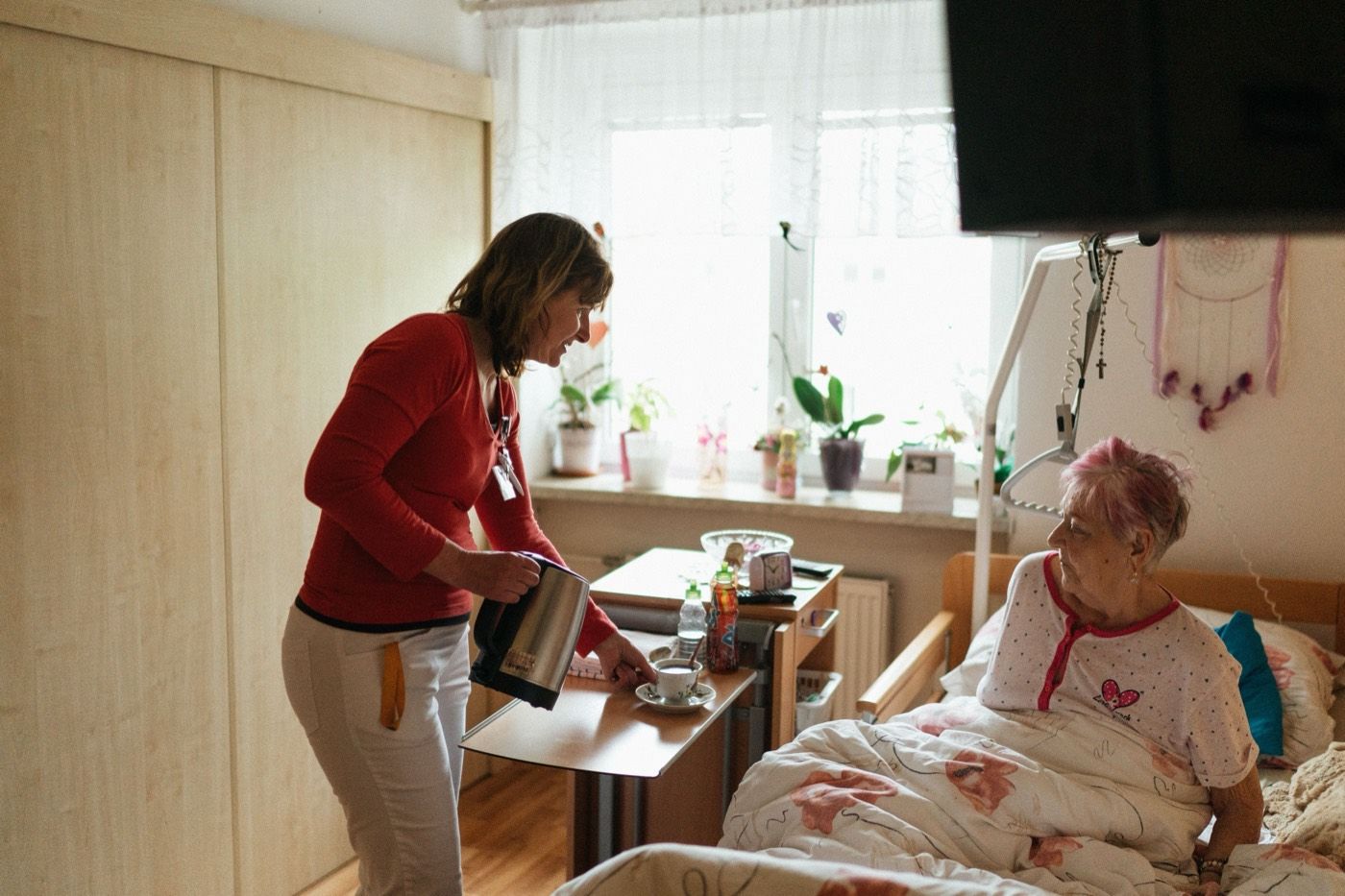 A caregiver bringing a cup of tea to a resident resting in bed