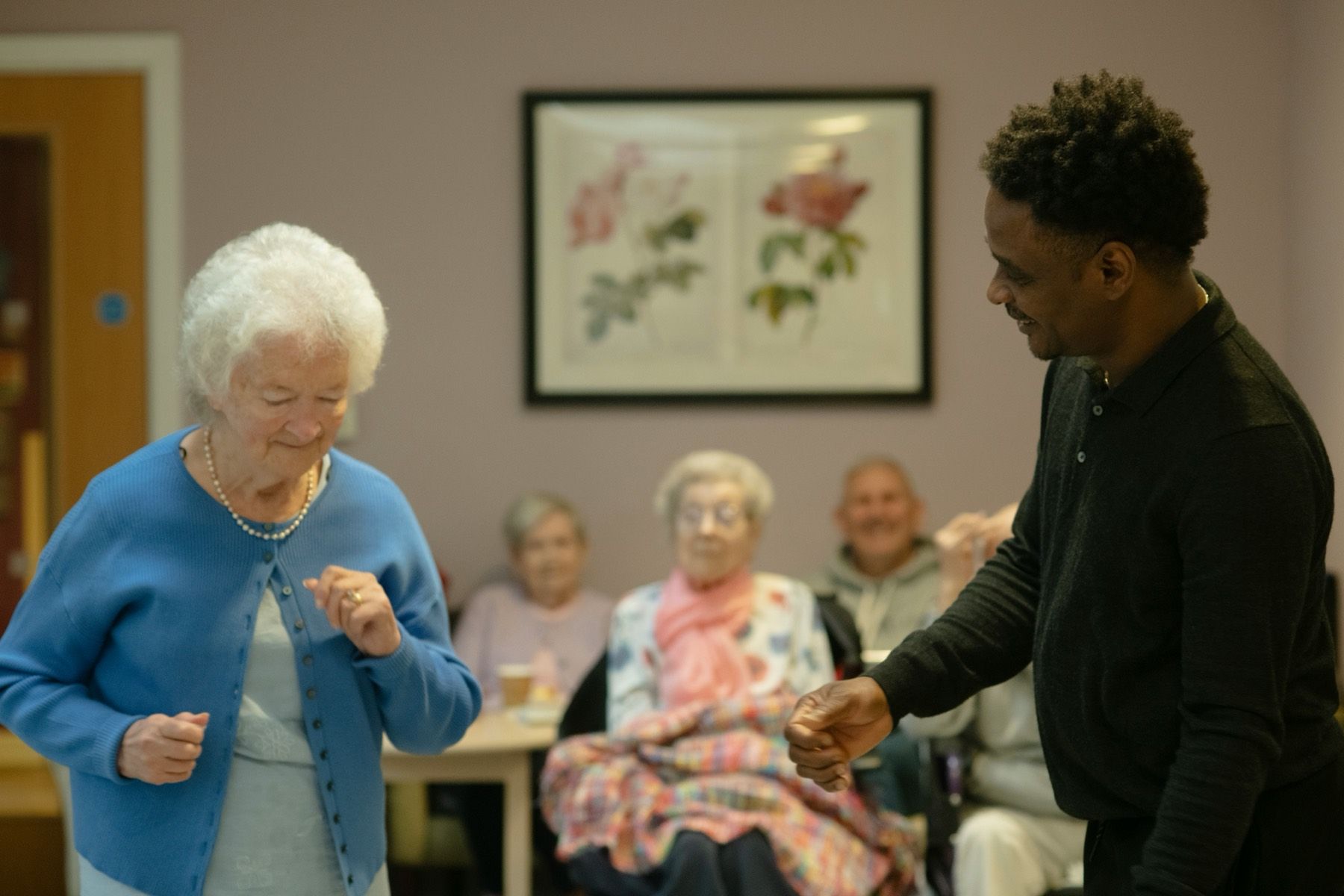 A caregiver and a resident dancing together while other residents smile in the living room